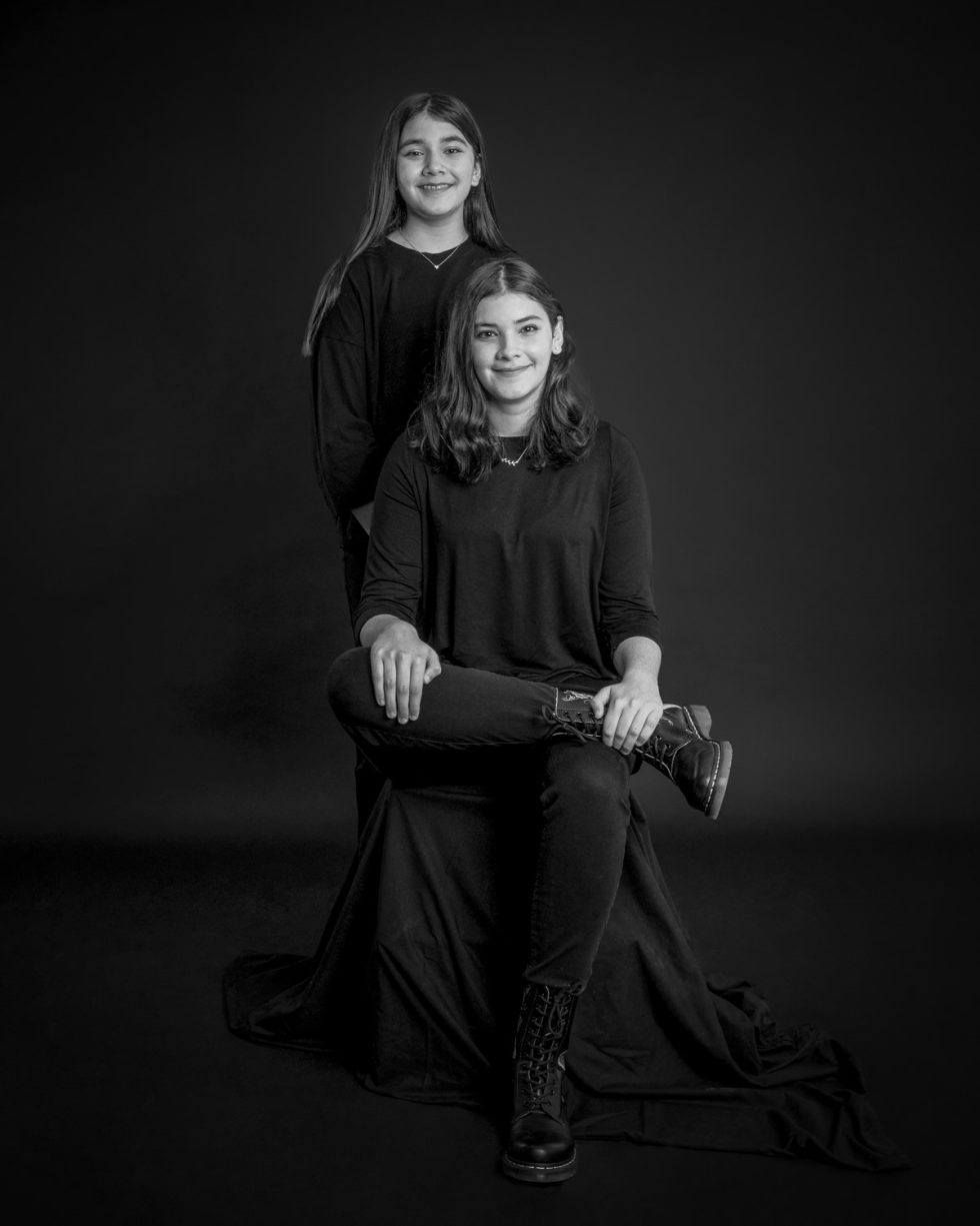 Black and white studio portrait of a woman seated wearing black and a young man standing behind her, both smiling at the camera.