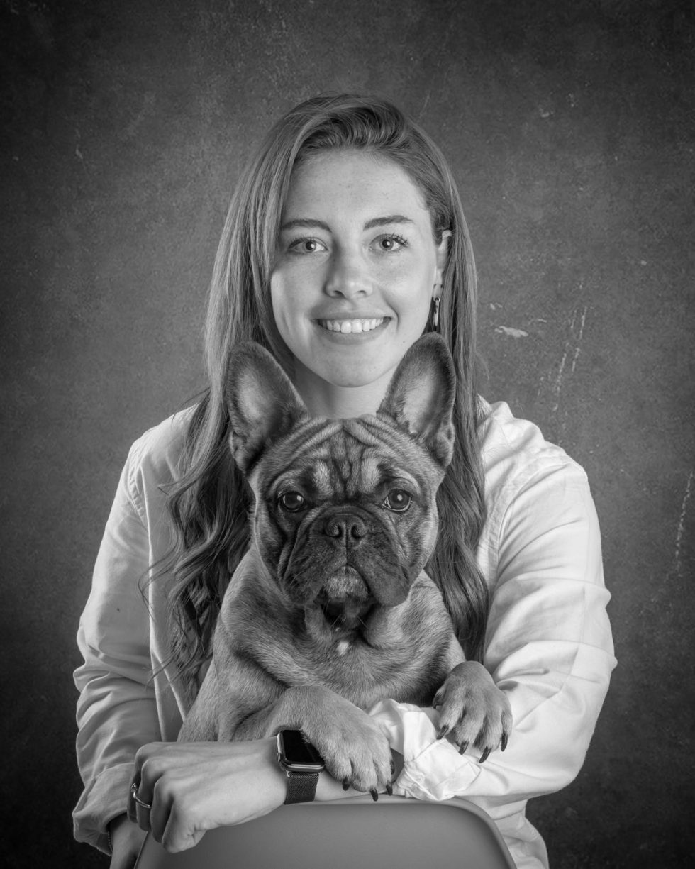 Black and white portrait of a smiling woman holding a french bulldog, both looking directly at the camera.