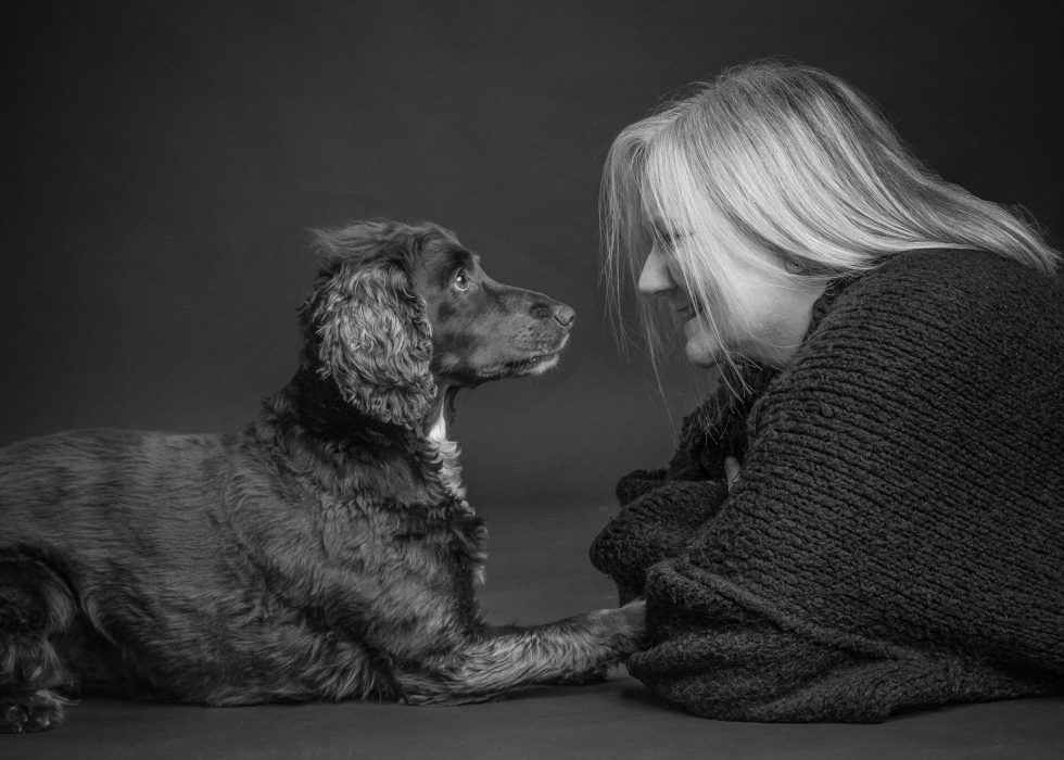 A woman and a brown dog sitting face to face in a black and white photograph, portraying a moment of silent communication.